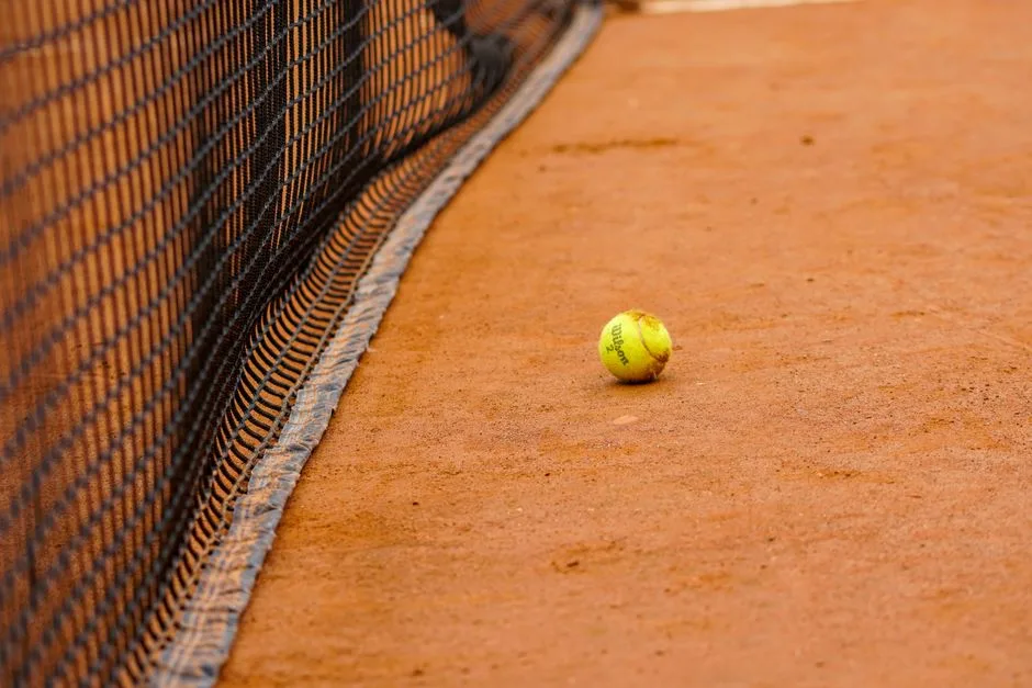 Primer plano de una pelota de tenis descansando en una pista de tierra batida cerca de la red, capturando la esencia del deporte.