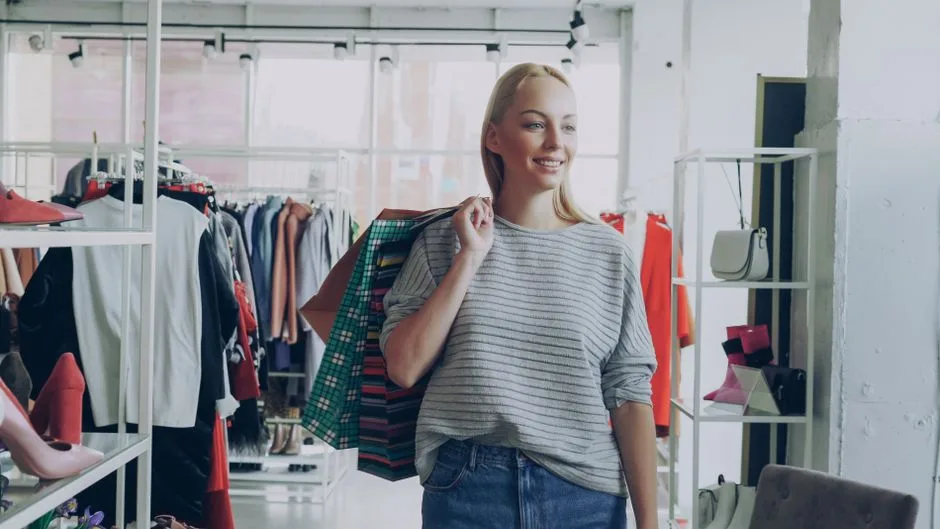 Mujer feliz sosteniendo bolsas de compras en una boutique de moda, mostrando la terapia de compras.