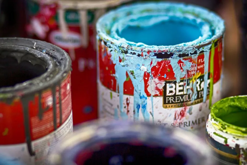 Primer plano de latas de pintura vibrantes y desordenadas, abiertas, con manchas coloridas en la superficie de un taller.
