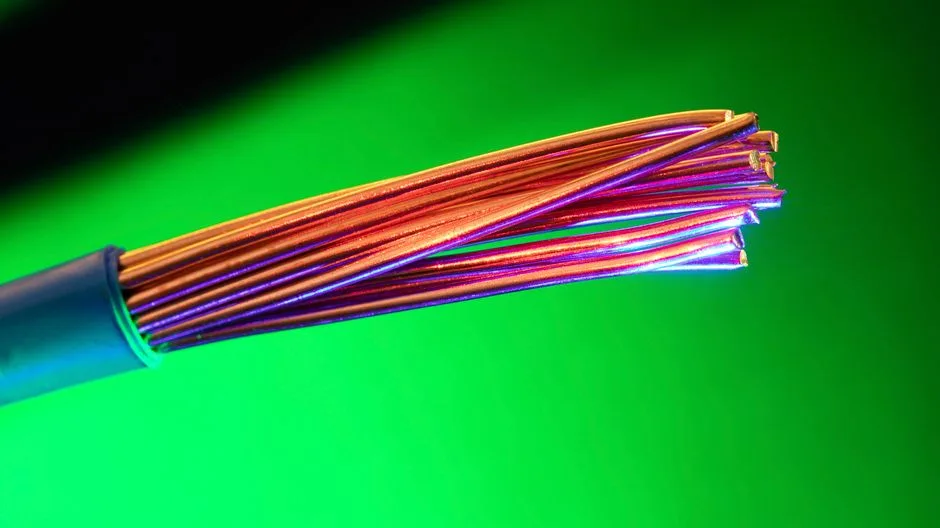 Primer plano de cables eléctricos de cobre coloridos sobre un fondo verde vibrante, mostrando contrastes y texturas vívidas.