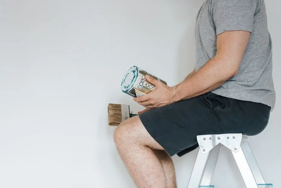 Hombre adulto sentado en una escalera sosteniendo una lata de pintura, preparándose para una renovación del hogar en interiores.